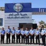 Line of uniformed police officers standing in a row outside a blue-and-white building with Arabic signage and a crest above the entrance.