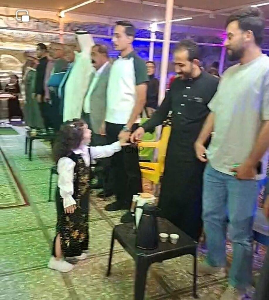 to1 - Center News Network Young girl in a sparkly vest shakes hands with a man in black as others line up during a social gathering in a decorated hall.
