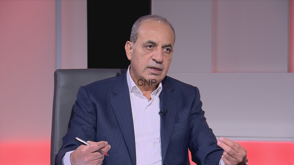 image - Center News Network Middle-aged man in a navy pinstripe suit and white shirt sits on a TV talk-show set, gesturing with his hands as he speaks (watermark 'CNP' on chest).