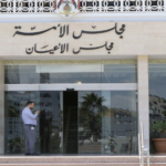 Man in gray clothing stands at the glass entrance of a government building, Arabic signage above the doors, and 'CNP' on the door.