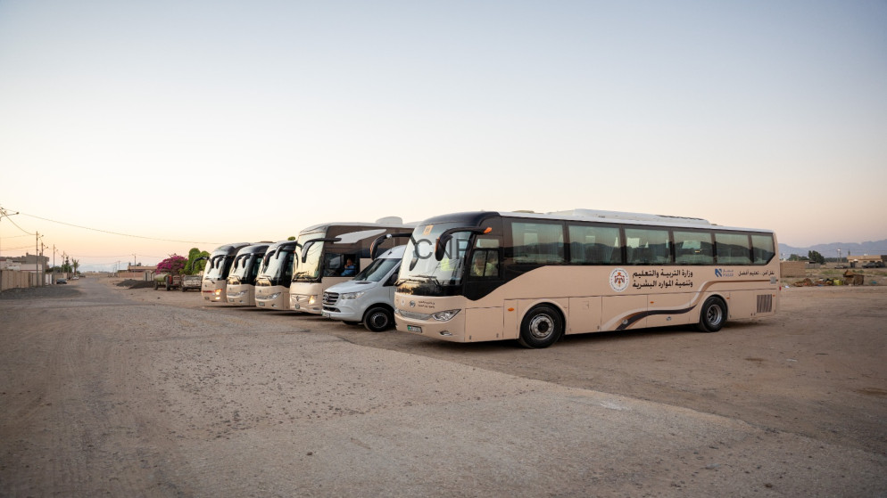 Row of beige buses parked in a dusty lot at sunset, with Arabic signage on the side.