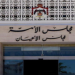 Facade of a government building featuring Arabic signage above glass doors and a crest, with decorative lattice panels at the top.
