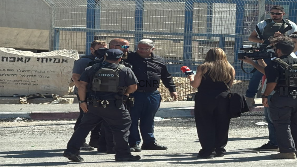 image - Center News Network Group of police officers in tactical vests interview a man while a female reporter with a red microphone films nearby, at a fenced area