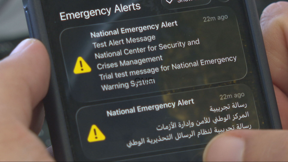 image - Center News Network Smartphone screen showing two National Emergency Alerts with yellow warning icons and bilingual English/Arabic text.