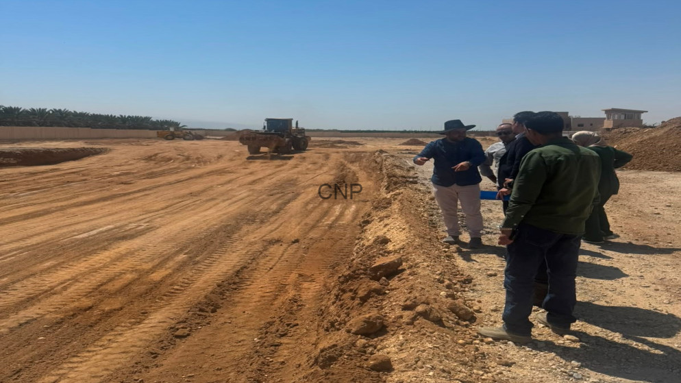 image - Center News Network Construction site scene with a bulldozer on a dirt road as a group of workers discuss along the edge of the excavation area.