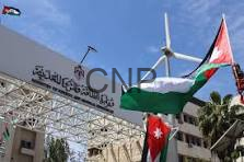 Outdoor event stage with a metal truss, Arabic banner, and Jordan and Palestinian flags waving against a blue sky.