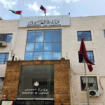 Exterior view of the Ministry of Labour building with Arabic and English signage, flags, and a glass facade behind a wooden entrance canopy.