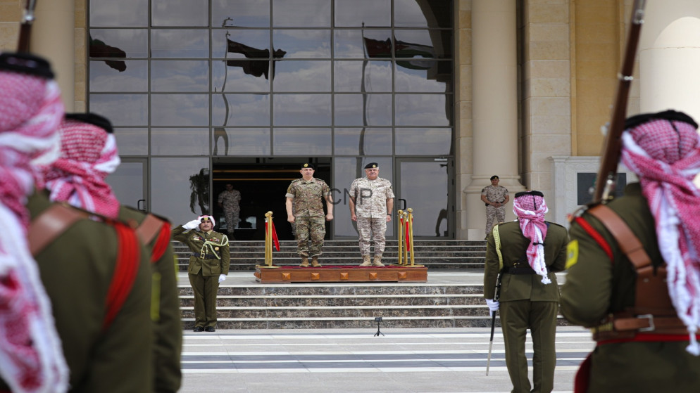 image - Center News Network Military officers stand on a wooden platform at the top of stone stairs in front of a glass-fronted building during a formal ceremony, with guards in the foreground.