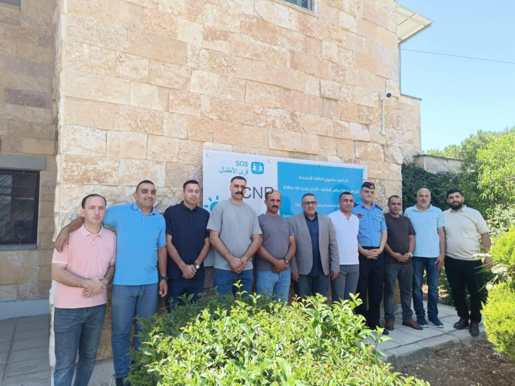 image - Center News Network Twelve men standing in a row outside a stone building, next to a blue project banner.