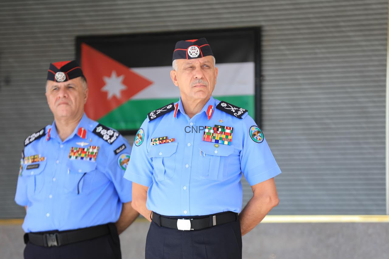 Two Jordanian security officers in ceremonial blue uniforms with medals, standing in front of a Jordanian flag.