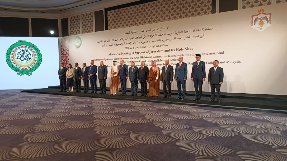 image - Rakeen News Group of officials in formal attire standing on a stage for a ministerial meeting photo, with a white banner and emblem on the wall behind them.