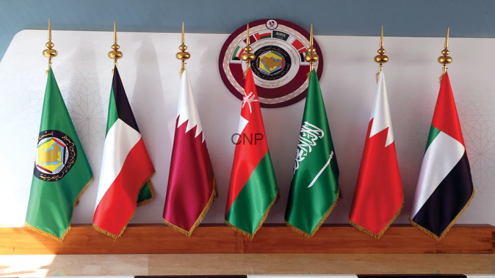 Seven national flags on a wooden podium with gold finials, arranged in a row in front of a wall with a circular seal.