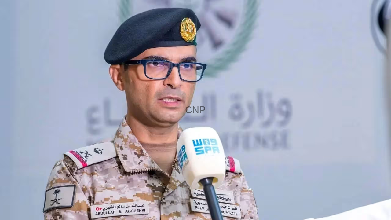 image - Center News Network Military officer in desert camouflage uniform and black beret speaking into a handheld mic at a press briefing, wearing glasses.