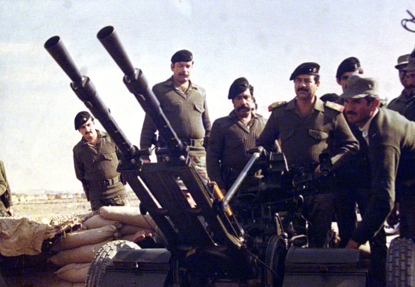 image - Center News Network Soldiers in uniform man large mounted artillery guns on a military vehicle in a desert with sandbags nearby.