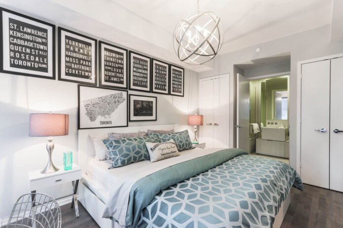 Modern bedroom with white furniture, teal geometric bedding, and a gallery wall of black-and-white framed prints.