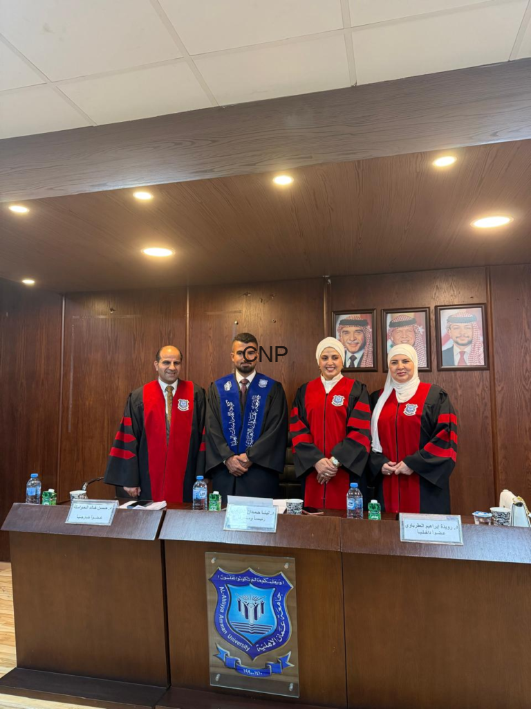 Four academics in red-and-black robes stand behind a wooden panel at a formal ceremony, with framed portraits on the wall behind them and a university crest on the front panel.