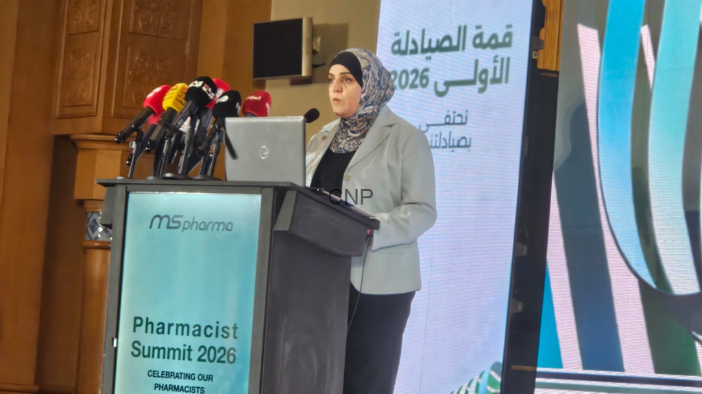 Woman in a gray blazer speaks at a podium with multiple microphones during the Pharmacist Summit 2026.
