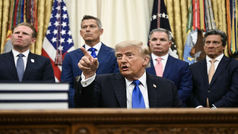 image - Center News Network Man in a dark suit and blue tie points with his index finger while seated at a desk, flanked by four suited men and U.S. flags in the background.