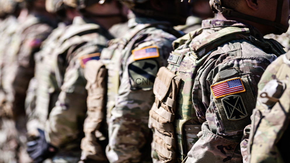 image - Center News Network Line of soldiers in camouflage gear with American flag patches, standing at attention.